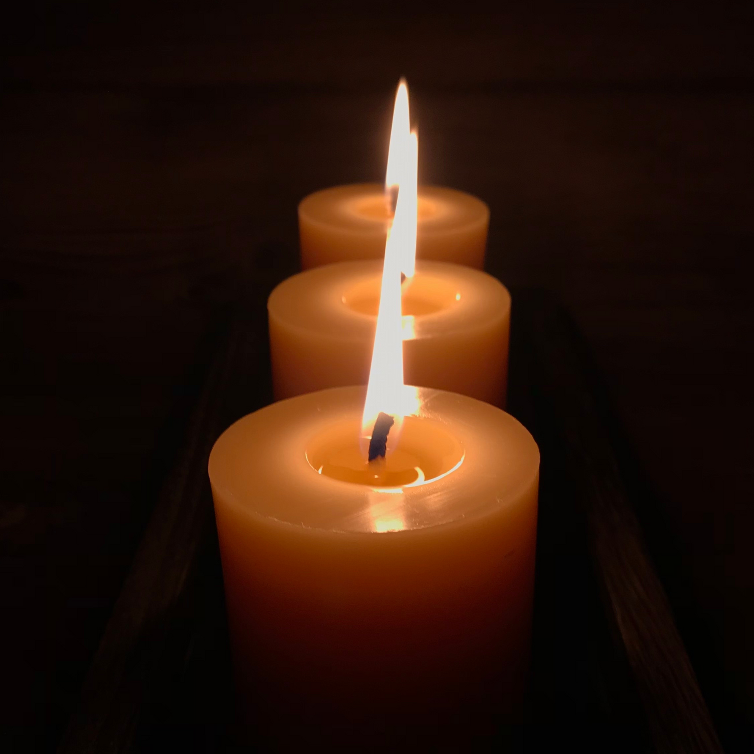 Three lit beeswax candles with a dark background