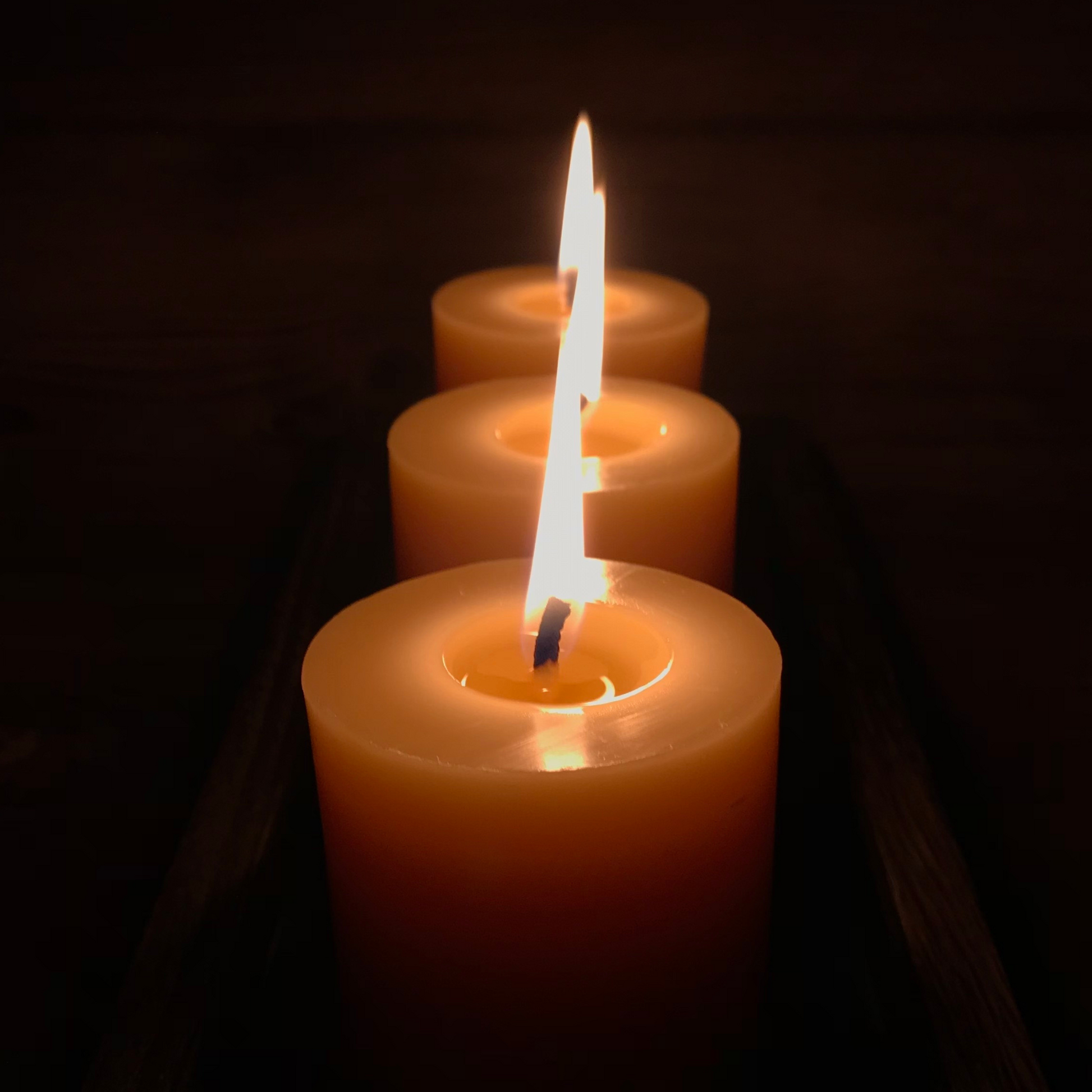 Three lit beeswax candles with a dark background