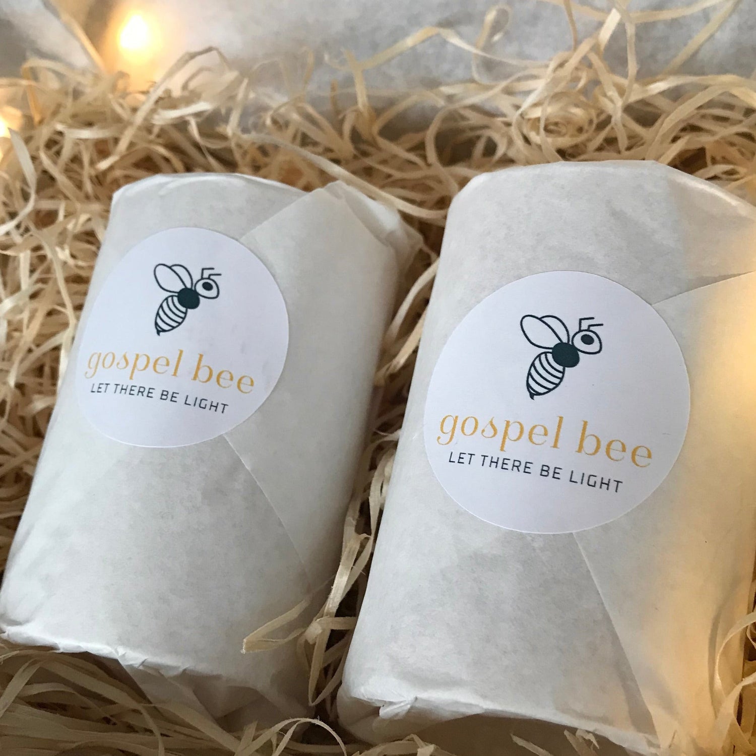 Two wrapped candles with brand labels on a bed of straw.