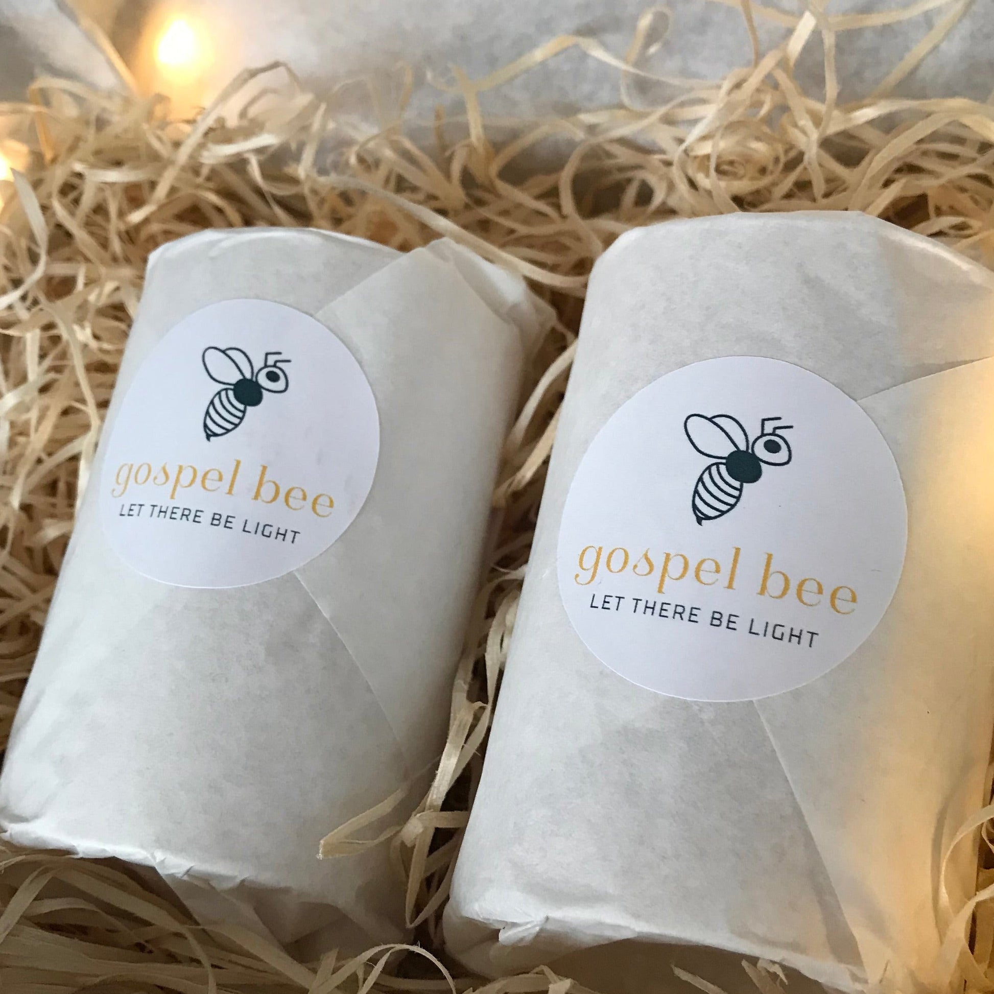 Two wrapped candles with brand labels on a bed of straw.