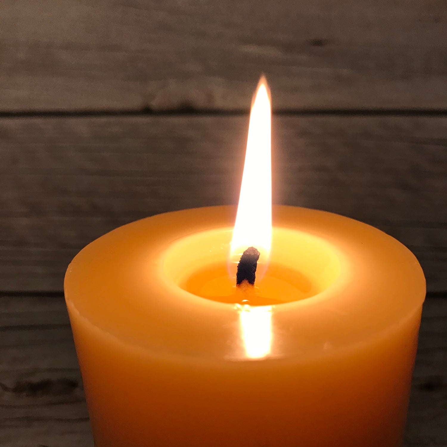 Yellow candle with a lit wick against a wooden background