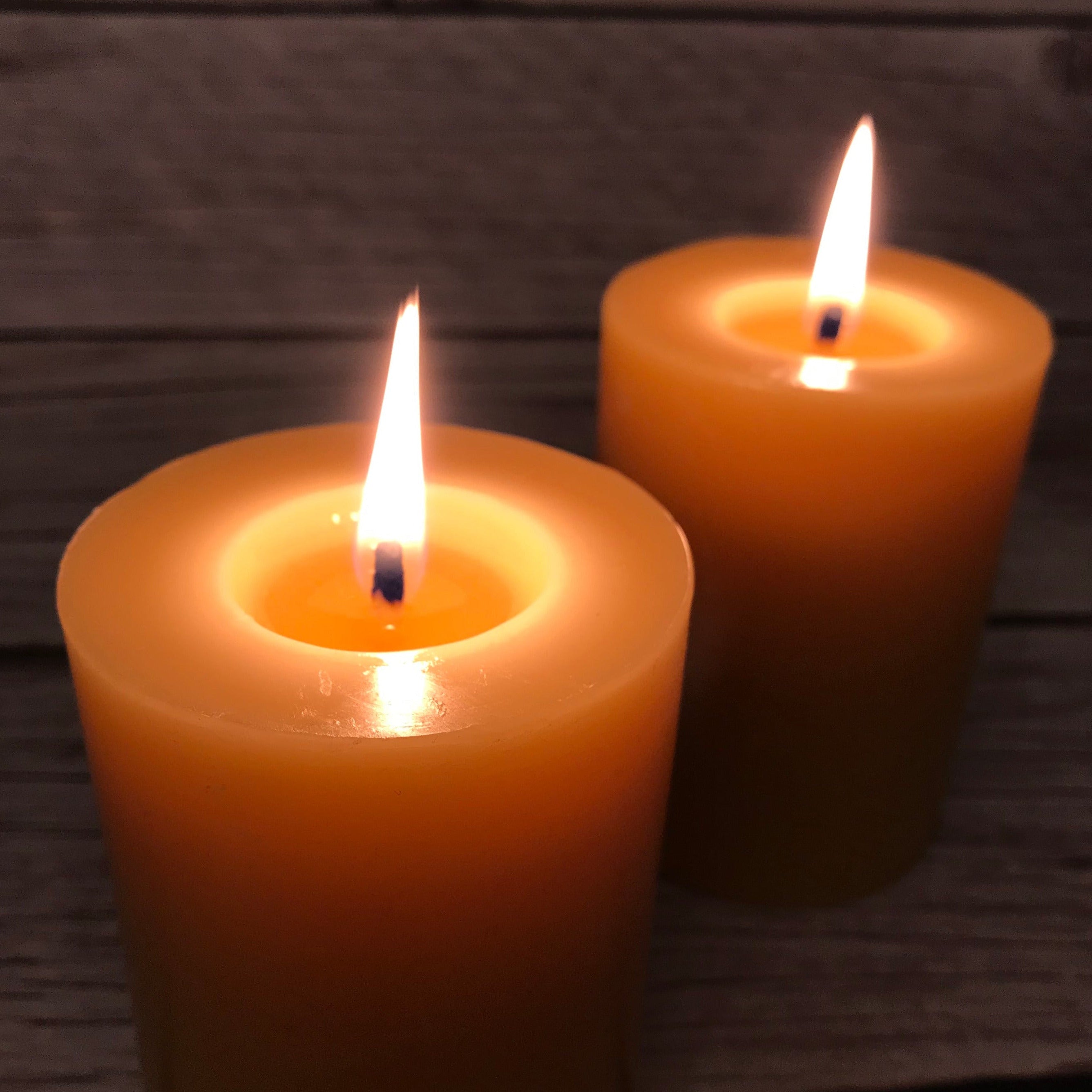 Two lit beeswax candles on a wooden surface