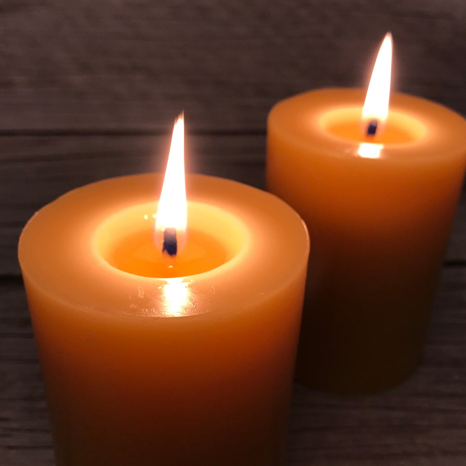 Two lit beeswax candles on a wooden surface with a dark background